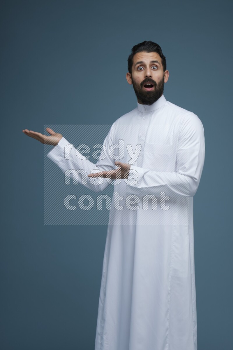 A man pointing in a blue background wearing Saudi Thob