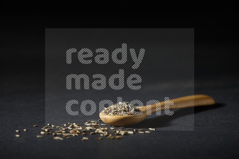 A wooden spoon full of cumin seeds on black flooring