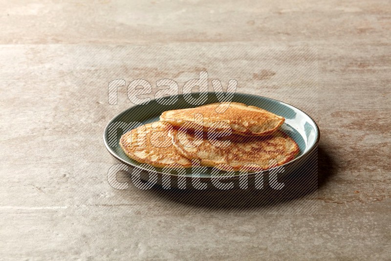 Three stacked plain pancakes in a blue plate on beige background