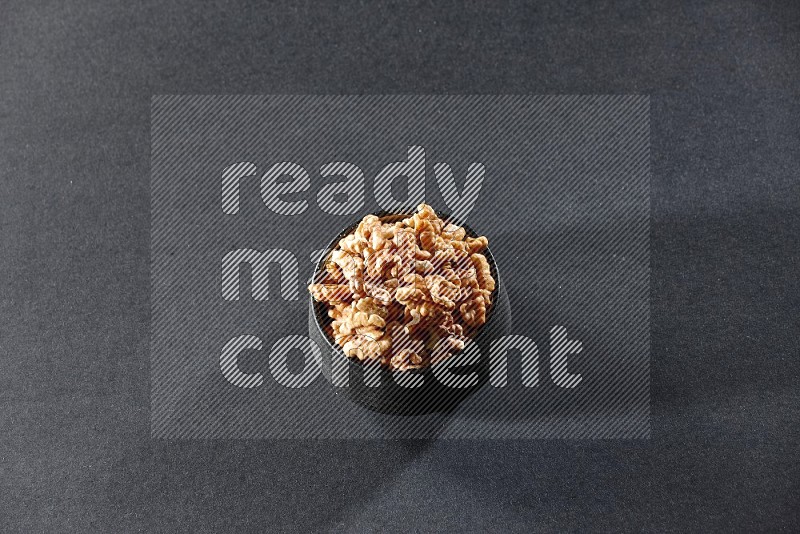 A black pottery bowl full of peeled walnuts on a black background in different angles