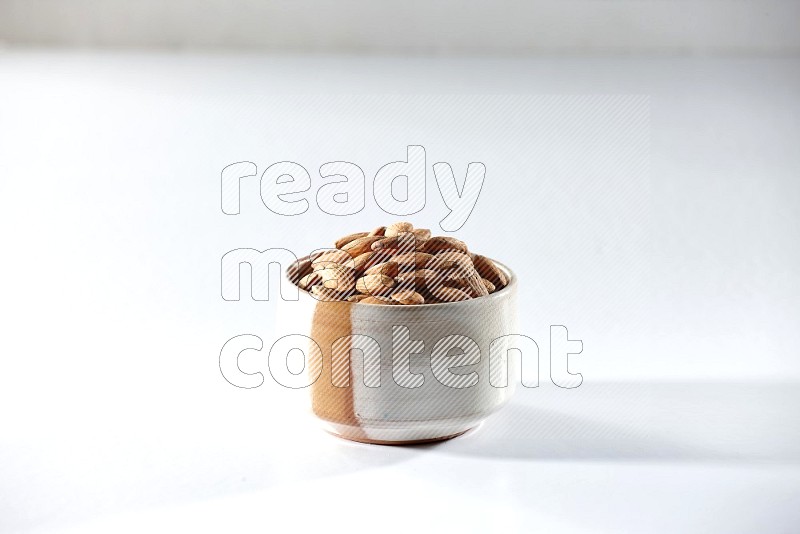 A beige ceramic bowl full of peeled almonds on a white background in different angles