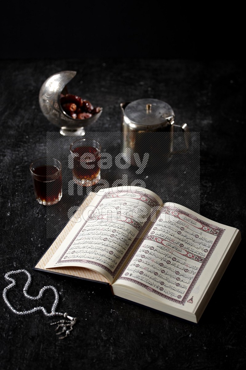 Moshaf with tea cups and prayer beads in a dark setup