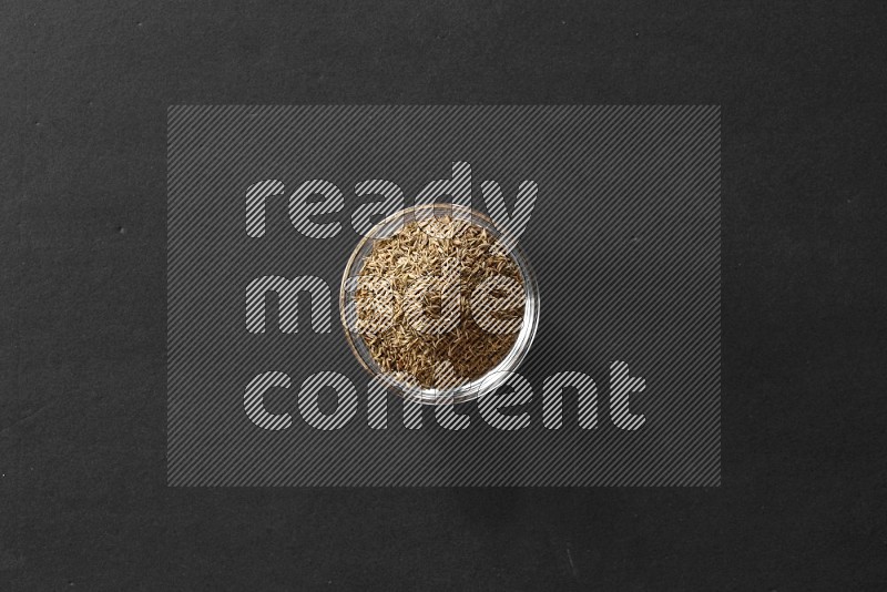 A glass bowl full of cumin on black flooring