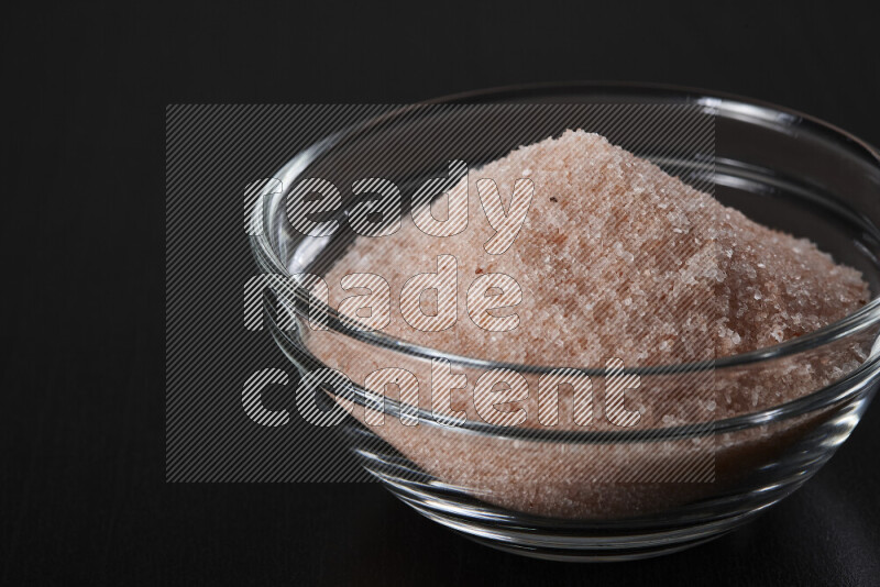 A glass bowl full of fine himalayan salt on black background