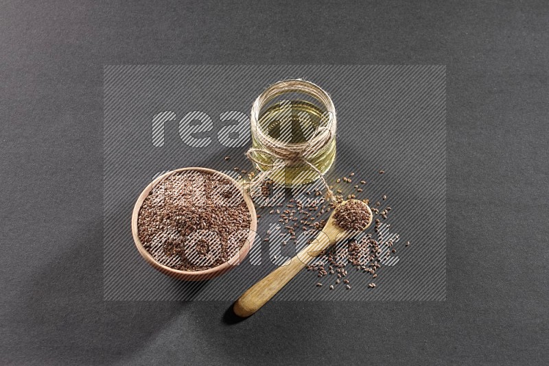 A wooden bowl and spoon full of flax and a glass jar of flax oil on a black flooring in different angles