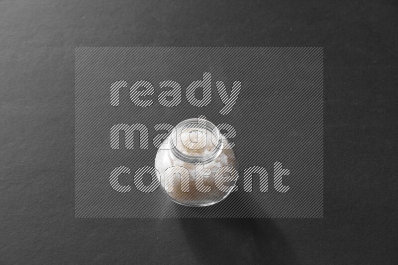 A glass spice jar full of salt on black flooring