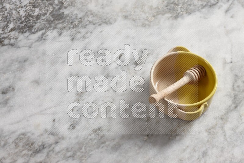 وعاء فخاري متعدد الألوان مع ملعقة عسل خشبية بداخله على خلفية من الرخام الرمادي