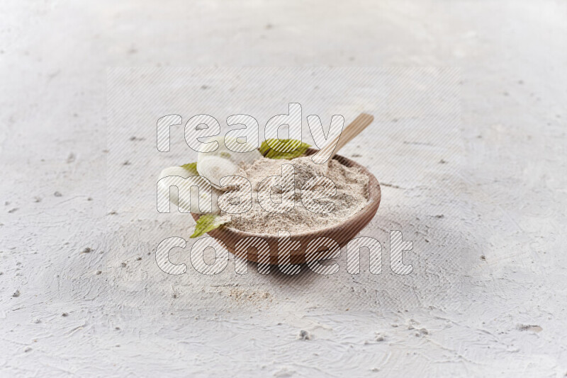 A wooden bowl full of onion powder with a wooden spoon in it with some sliced onions on white background