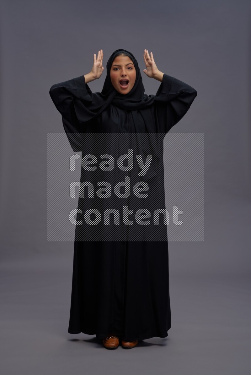 Saudi woman wearing Abaya standing hands behind head on gray background