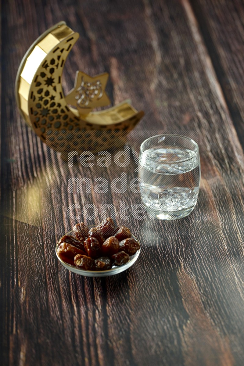 A crescent lantern with drinks, dates, nuts, prayer beads and quran on brown wooden background