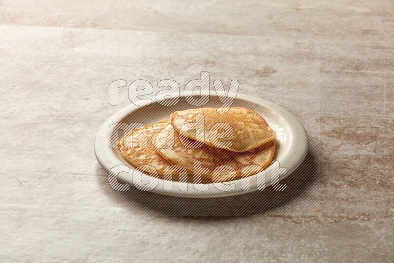 Three stacked plain pancakes in a beige plate on grey beige background