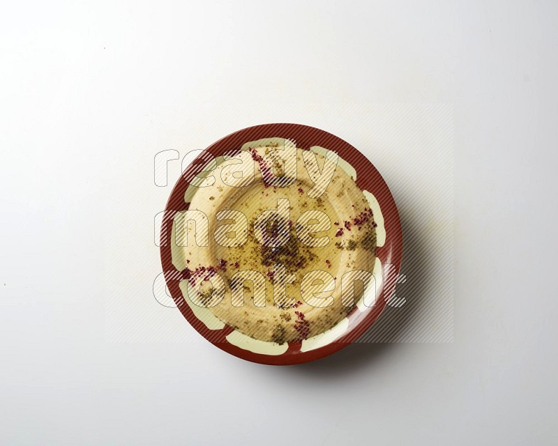 Hummus in a traditional plate garnished with zaatar & sumak on a white background