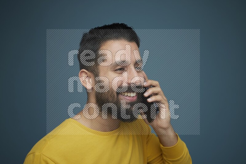 A man having a calling in a blue background wearing a yellow shirt