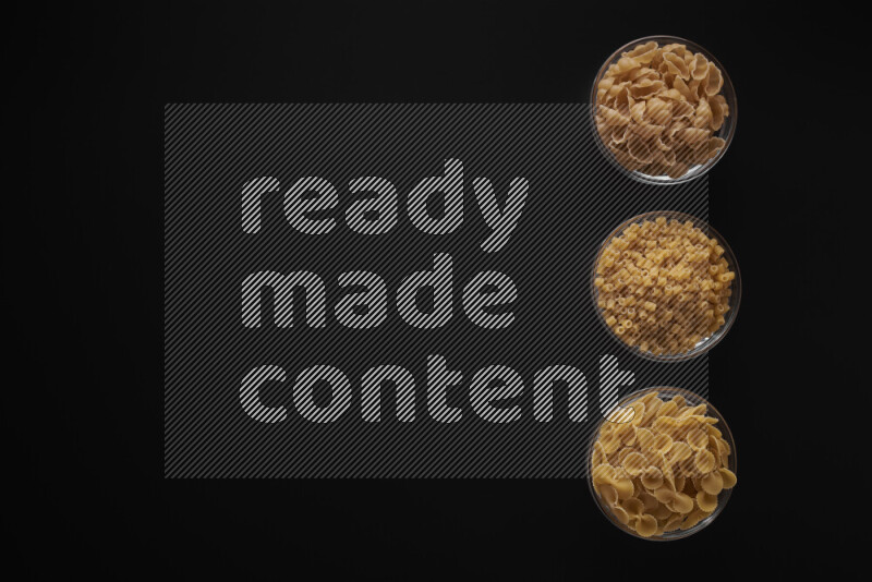 Different pasta types in 3 glass bowls on black background