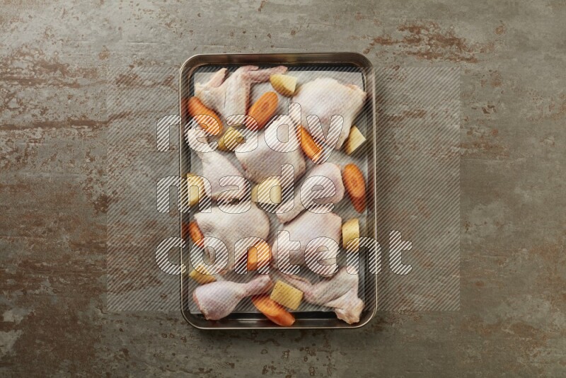 Mixed fresh chicken pieces in an oven tray on a textured rustic background