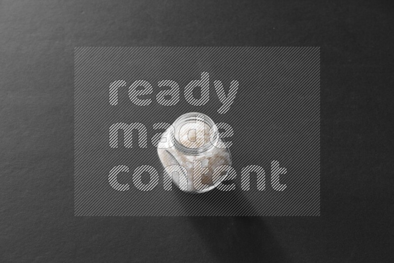 A glass spice jar full of salt on black flooring