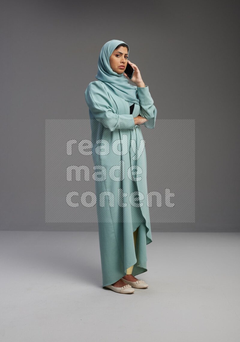 Saudi Woman wearing Abaya standing talking on phone on Gray background
