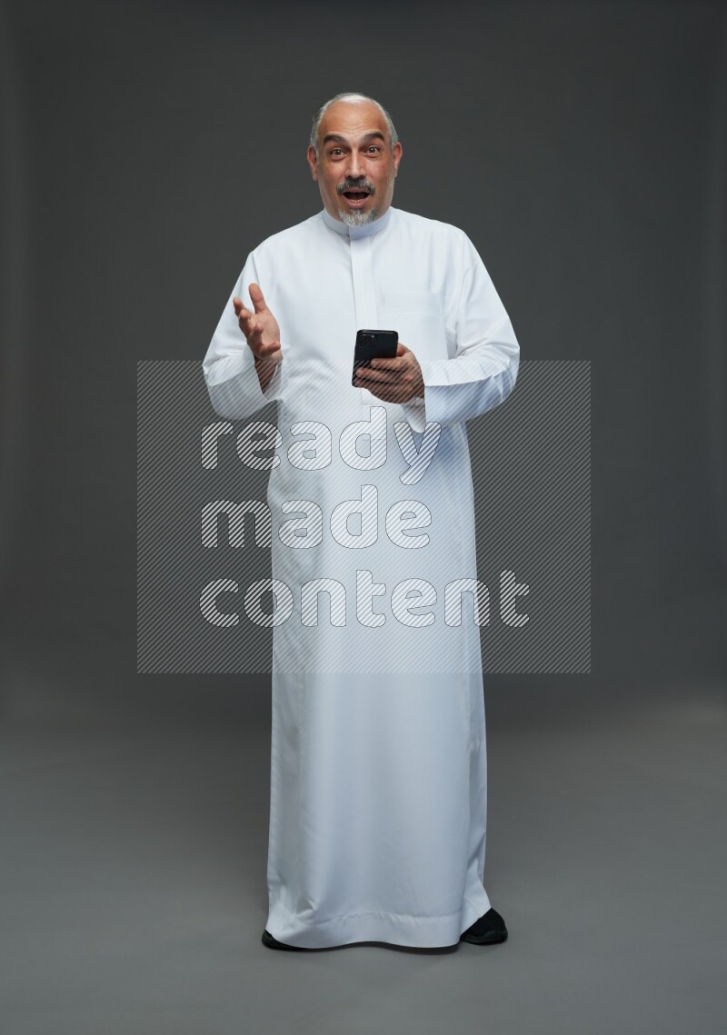 Saudi man without shomag Standing texting on phone on gray background