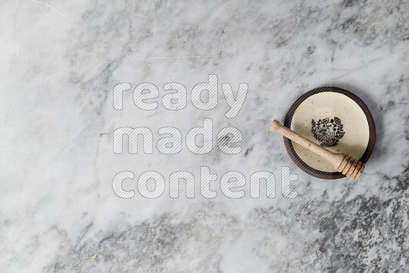 Decorative Pottery Plate with wooden honey handle in it, on grey marble flooring, Top View