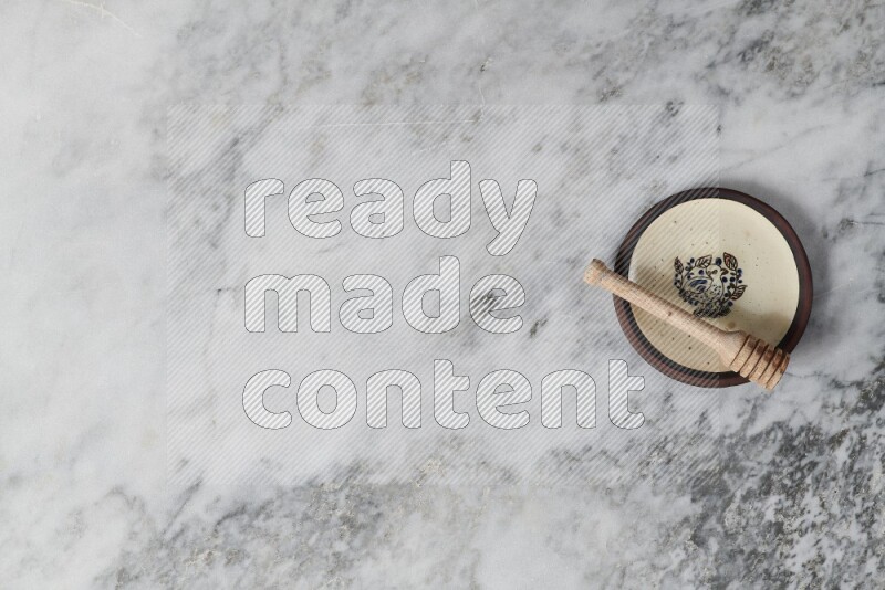 Decorative pottery plate with wooden honey dipper in it on grey marble background