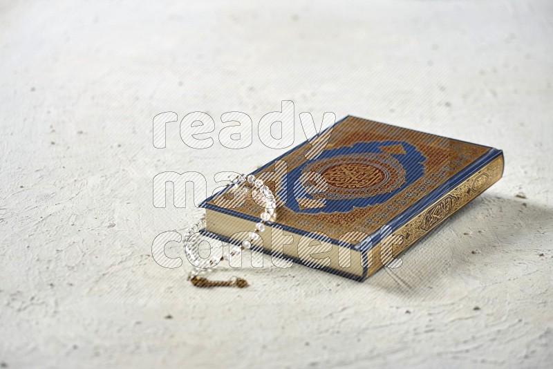 Quran with dates, prayer beads and different drinks all placed on textured white background