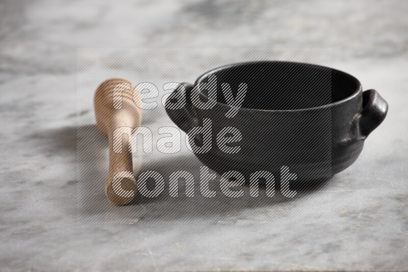 Black pottery bowl with wooden honey dipper on the side on grey marble background
