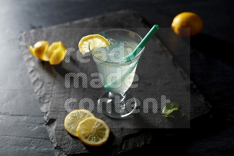 A glass of lemon juice with a straw on black background