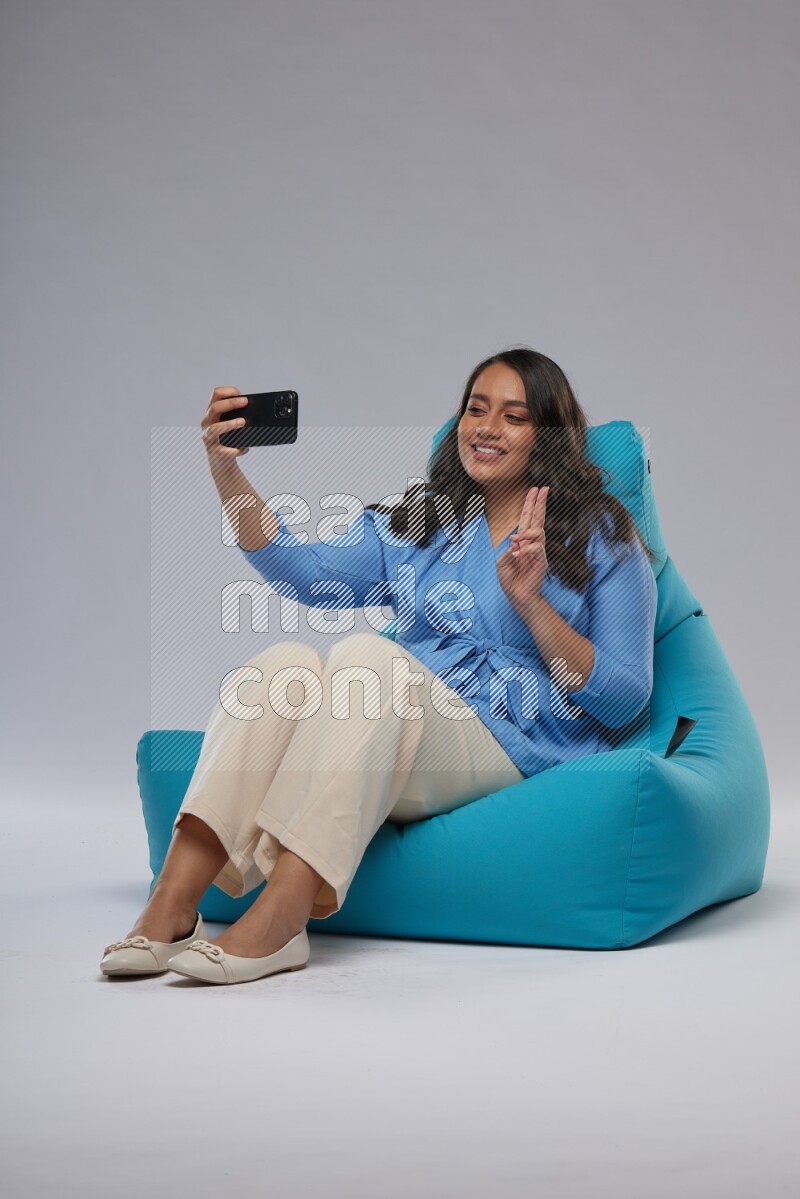 A woman sitting on a blue beanbag and taking selfie
