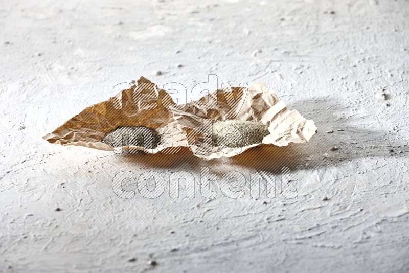 2 Crumpled pieces of paper full of black and white pepper powder on a textured white flooring