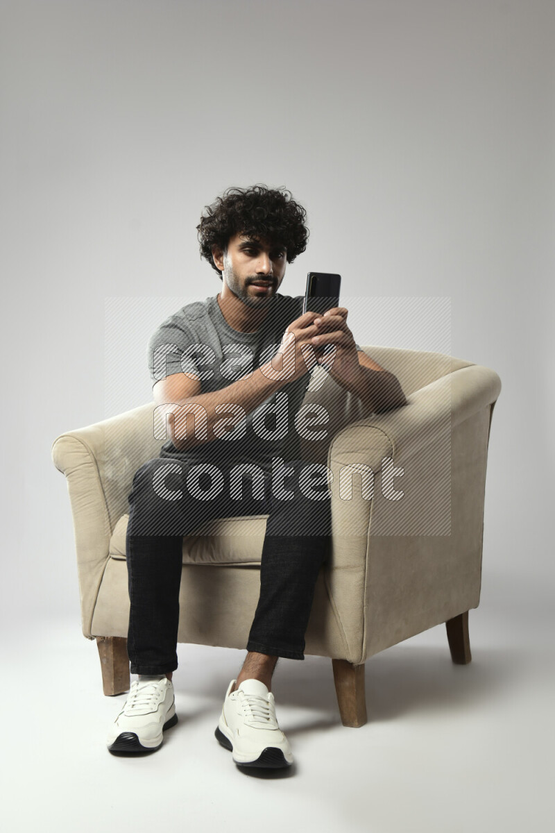 A man wearing casual sitting on a chair shooting with his phone on white background