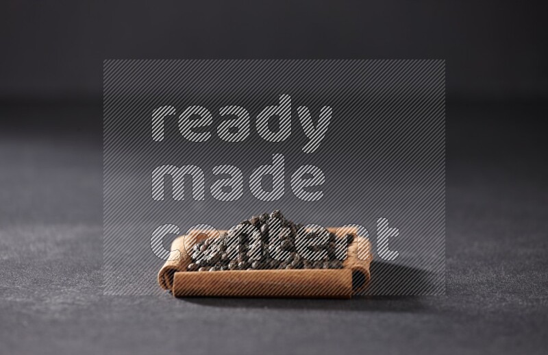 A single square of cinnamon sticks full of black pepper on black flooring