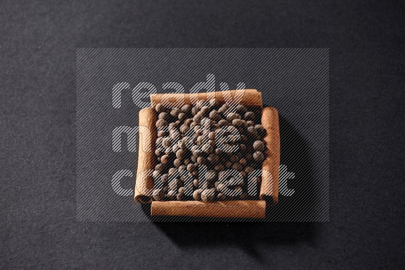 A single square of cinnamon sticks full of allspice on black flooring