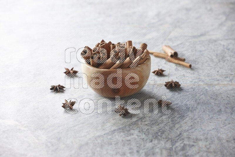 wooden bowl full of cinnamon sticks surrounded by star anis on marble background in different angles