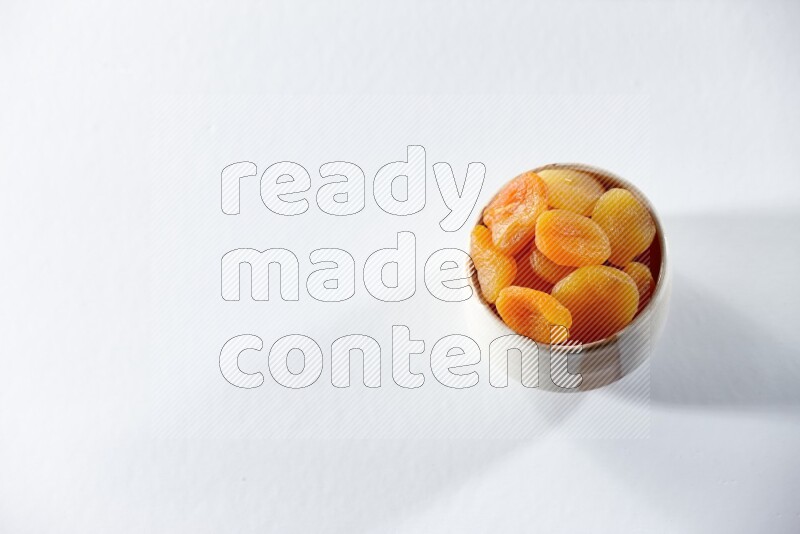 A beige ceramic bowl full of dried apricots on a white background in different angles