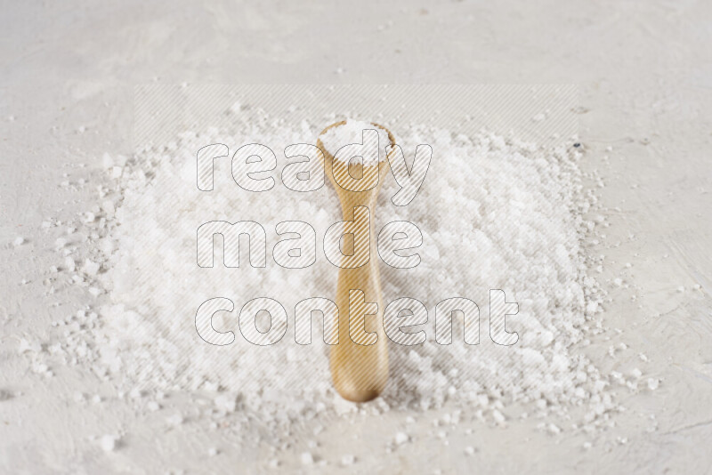 A wooden spoon full of white salt on white background