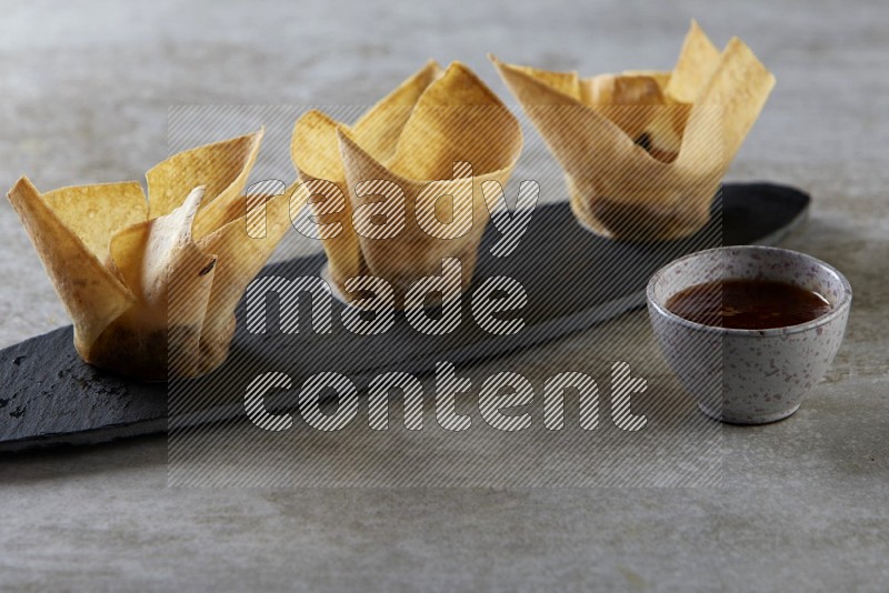 wonton cups with soy sauce ramkin on oval slate on grey textured counter top