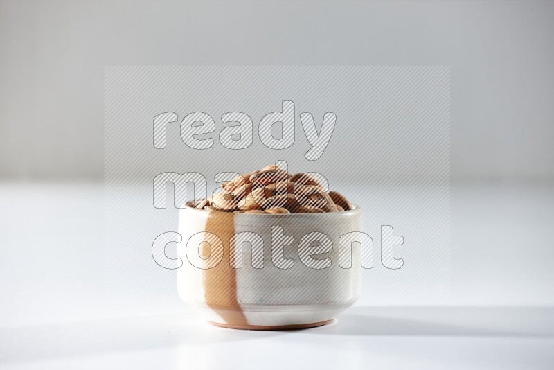 A beige ceramic bowl full of peeled almonds on a white background in different angles