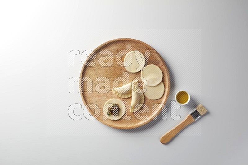 two closed sambosas and one open sambosa filled with meat while oil with oil brush aside in a wooden dish on a white background