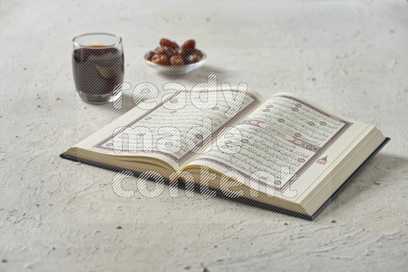 Quran with dates, prayer beads and different drinks all placed on textured white background