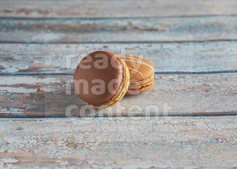 45º Shot of of two assorted Brown Irish Cream, and Yellow, and Brown Chai Latte macarons  on light blue background