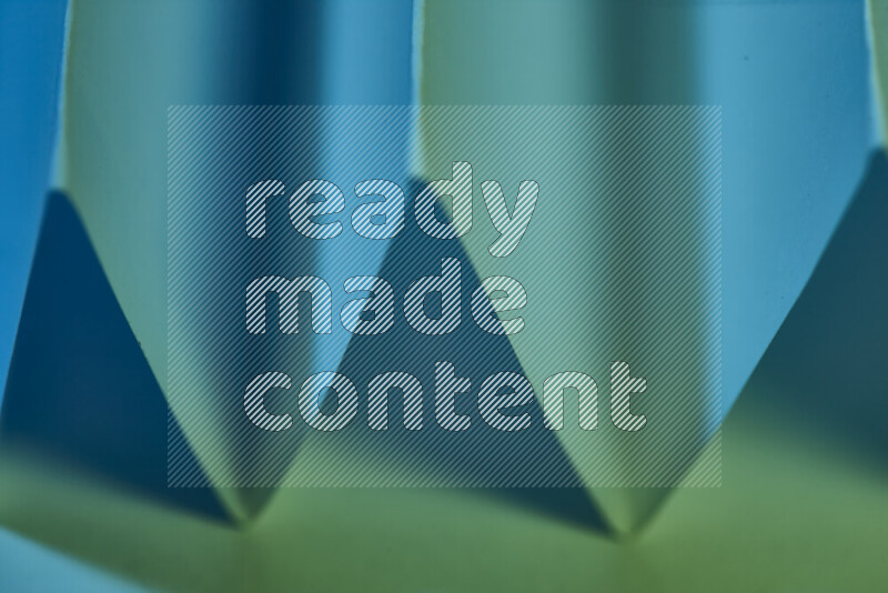 A close-up abstract image showing sharp geometric paper folds in green and blue gradients