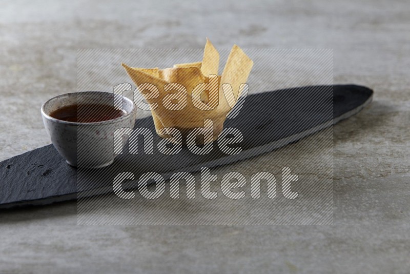 wonton cups with soy sauce ramkin on oval slate on grey textured counter top