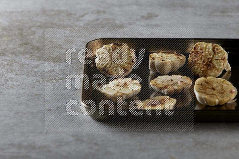half's roasted garlic in a stainless tray on a grey textured countertop