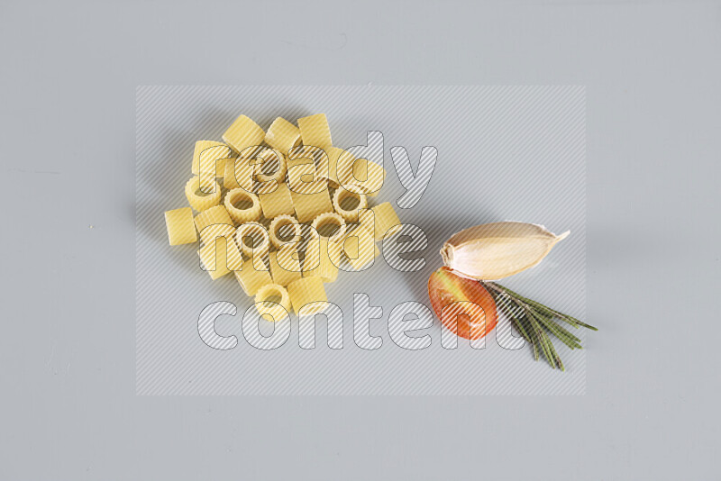 Raw pasta with different ingredients such as cherry tomatoes, garlic, onions, red chilis, black pepper, white pepper, bay laurel leaves, rosemary, cardamom and mushrooms on light blue background