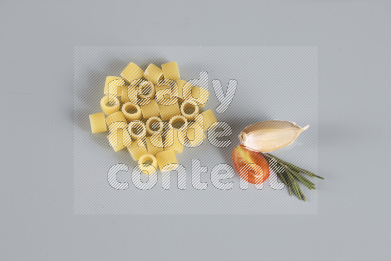 Raw pasta with different ingredients such as cherry tomatoes, garlic, onions, red chilis, black pepper, white pepper, bay laurel leaves, rosemary, cardamom and mushrooms on light blue background