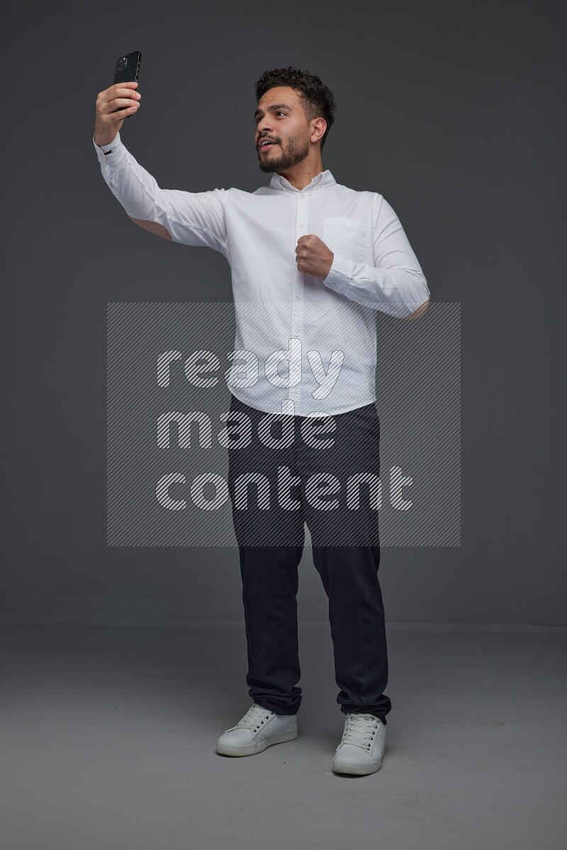 A man wearing smart casual and taking selfie with his phone eye level on a gray background