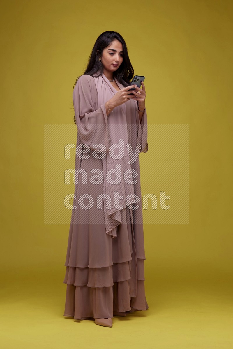 A woman Texting on a Yellow Background wearing Brown Abaya