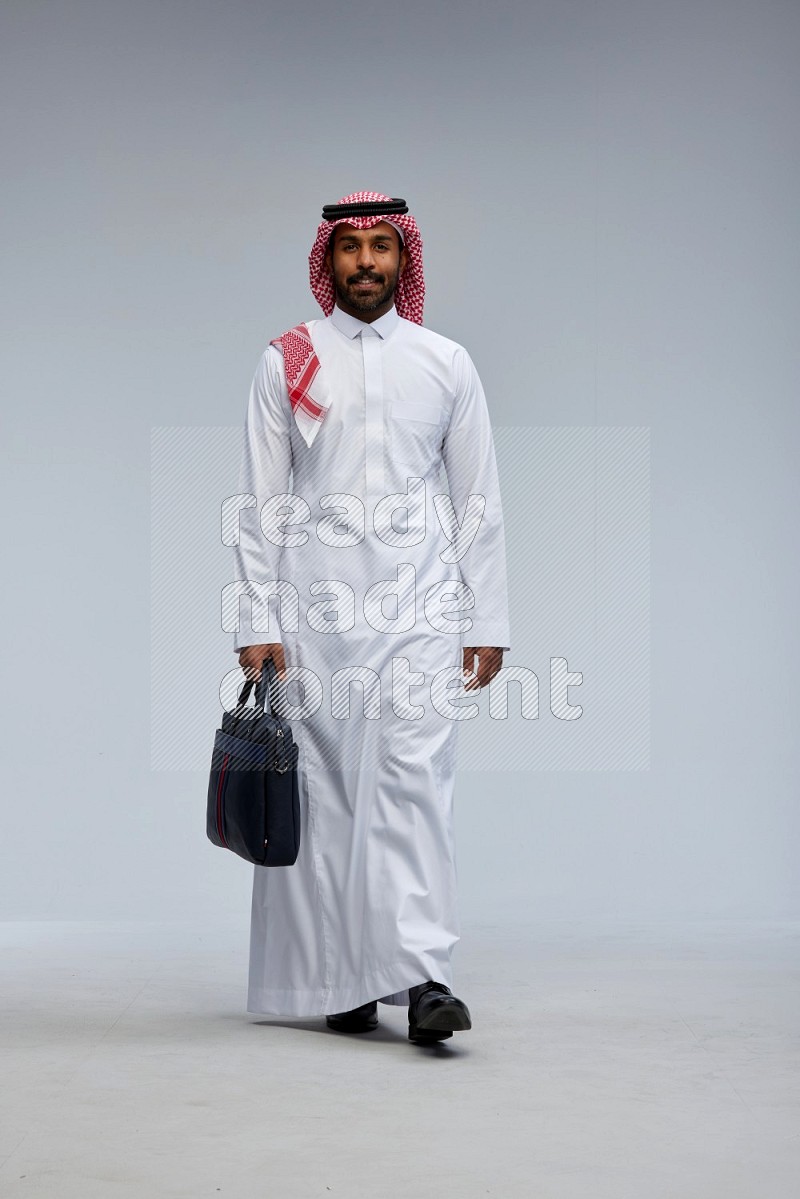 Saudi man Wearing Thob and shomag standing holding bag on Gray background