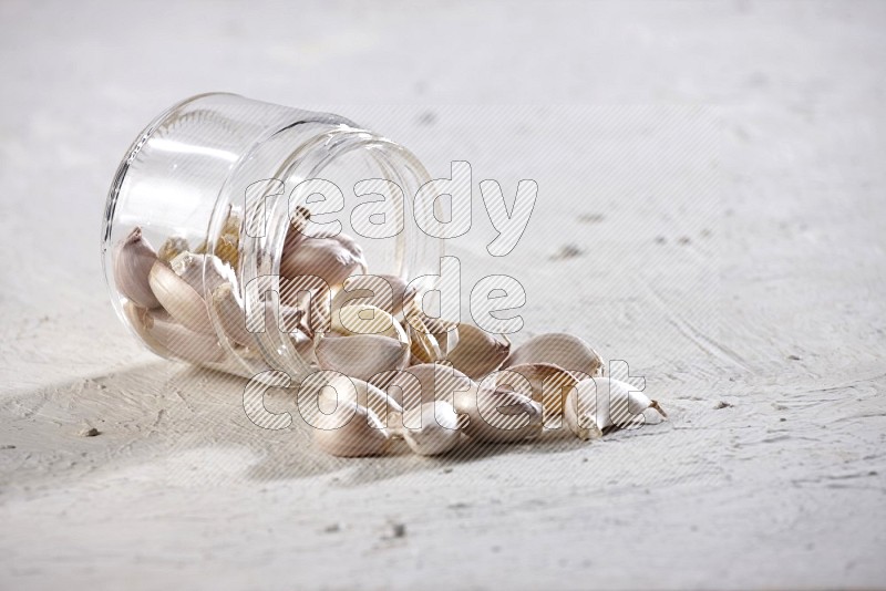 A glass jar full of garlic cloves flipped and the cloves came out on a textured white flooring in different angles