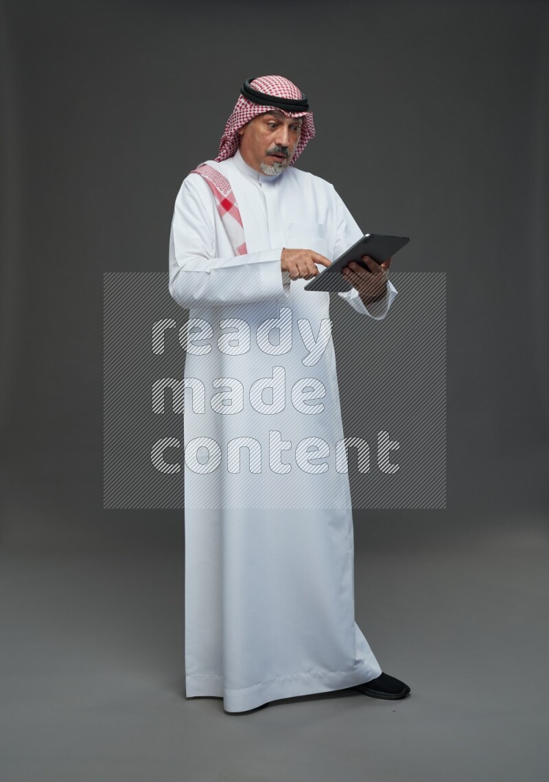 Saudi man with shomag Standing working on tablet on gray background